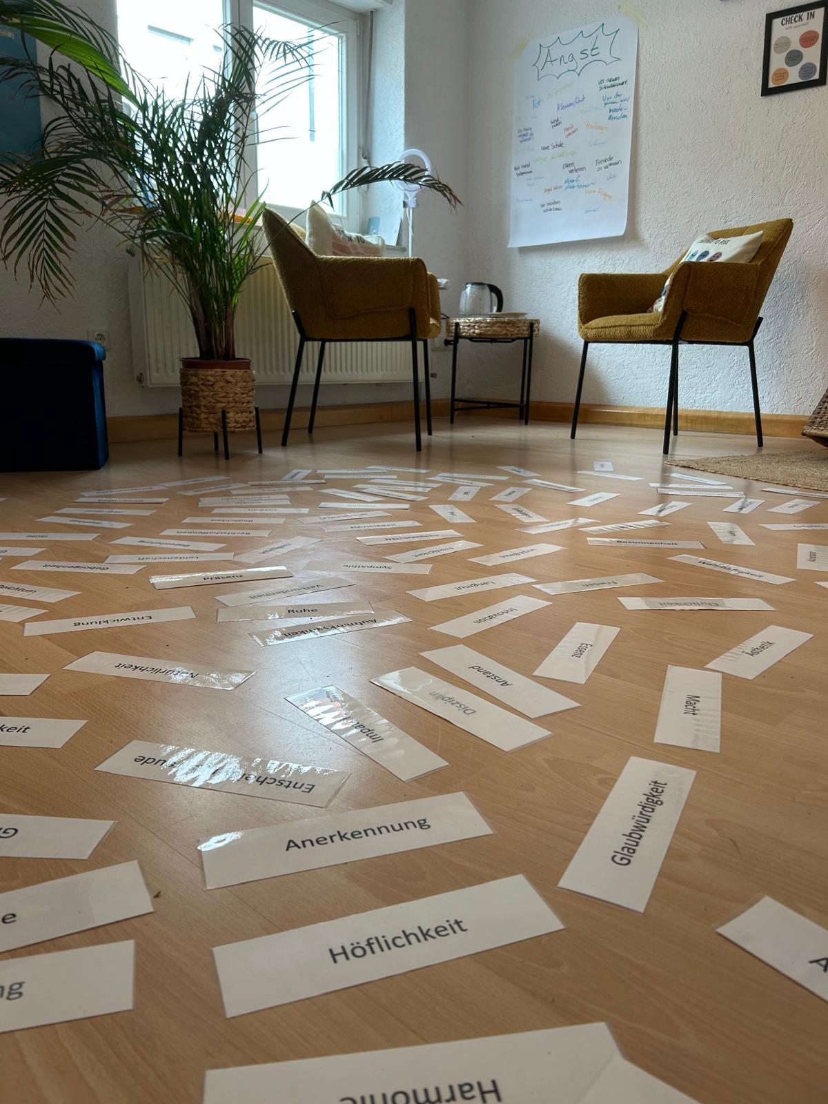 Raum der Glückspraxis mit Sesseln, Palme und vielen Wertekarten auf dem Boden
