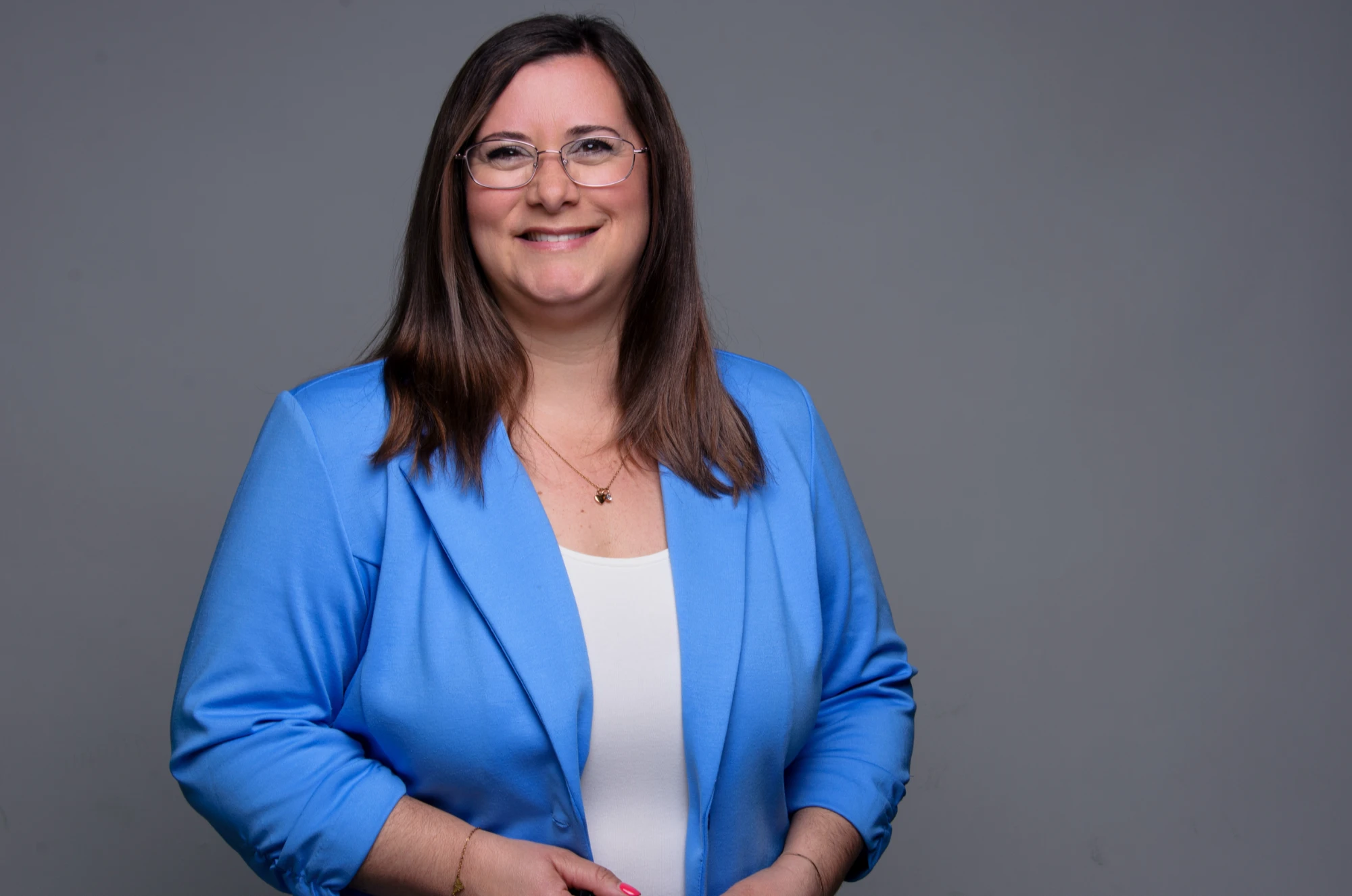 Dana Weber, lächelnd im hellblauen Blazer vor grauem Hintergrund
